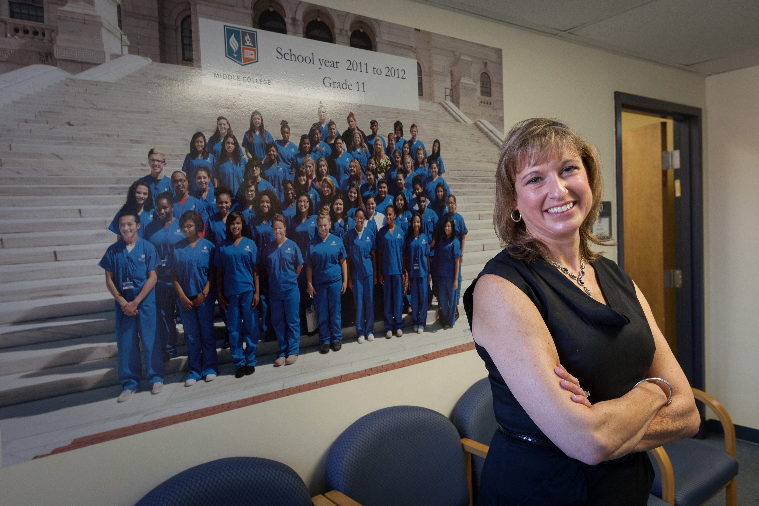 Pamela McCue, CEO of the R.I. Nurses Institute Middle College Charter School, in front of a poster of the first entering class of students from 2011.